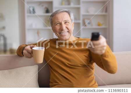 Senior man with coffee mug changing TV channels 113690311