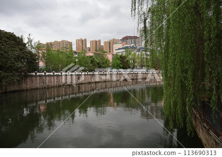 中國成都的城市景觀,河流、鮮綠色的柳樹、樹木和摩天大樓,天空、樹木和建築物倒映在河面上。 中國成都的城市景觀,河流、鮮綠色的柳樹、樹木和摩天大樓,天空、樹木和建築物倒映在河面上。 113690313