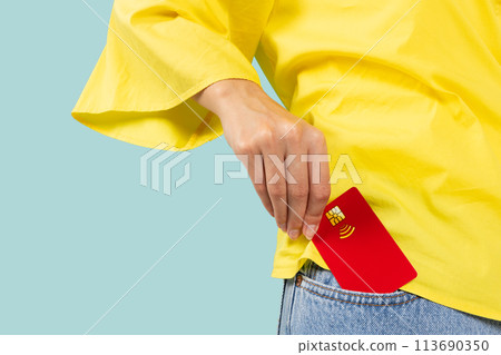 Close up photo shot of female hand putting credit bank card in jeans front pocket isolated on blue Close up photo shot of female hand putting credit bank card in jeans front pocket isolated on blue 113690350