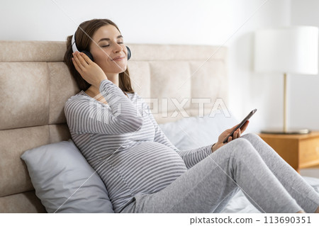 Pregnant woman relaxing with headphones at home Pregnant woman relaxing with headphones at home 113690351