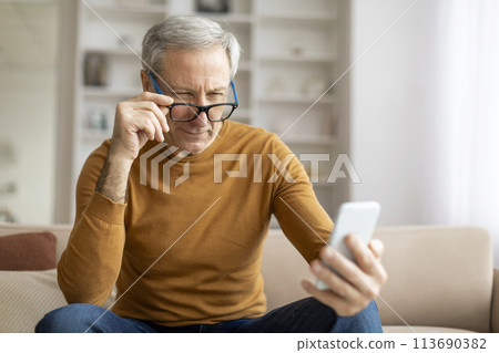 Senior man holding phone with a contemplative look 113690382