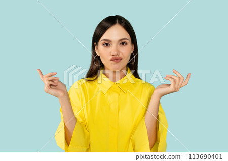 Confused serious young lady spreads arms to sides, does not know what to choose on blue studio background Confused serious young lady spreads arms to sides, does not know what to choose on blue studio background 113690401