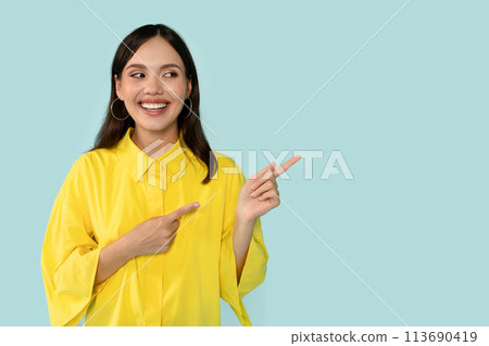 Happy Young Woman Pointing Aside At Copy Space on Blue Background Happy Young Woman Pointing Aside At Copy Space on Blue Background 113690419
