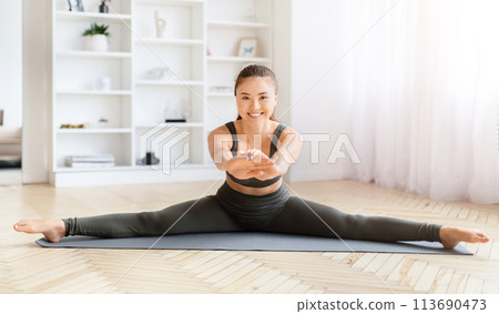 Woman performing a split stretch on yoga mat Woman performing a split stretch on yoga mat 113690473