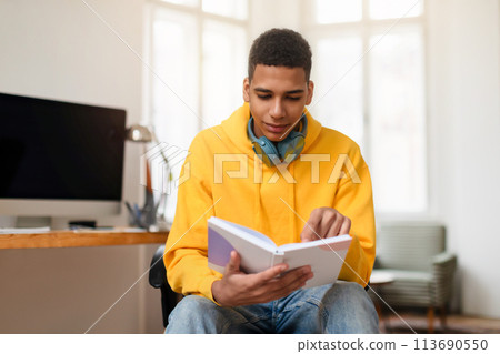 Young man reading a notebook at a home office desk Young man reading a notebook at a home office desk 113690550