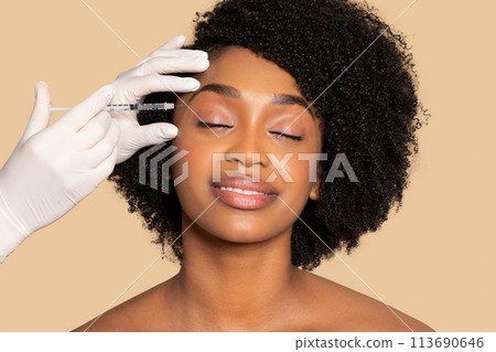 Relaxed black woman with syringe by face, aesthetic care Relaxed black woman with syringe by face, aesthetic care 113690646