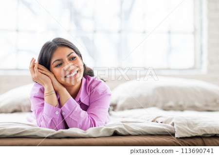 Smiling woman lying on bed resting her head 113690741