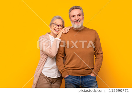 Happy Caucasian elderly couple embraces against yellow studio backdrop Happy Caucasian elderly couple embraces against yellow studio backdrop 113690771