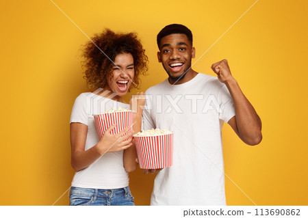 Emotional black couple enjoying movie with buckets of popcorn 113690862
