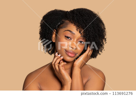 Graceful black woman with curly hair touches face, beige tone 113691276