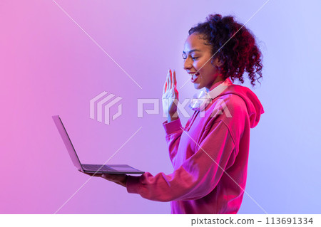 Woman in hoodie gesturing to open laptop screen 113691334