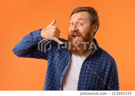 Cheerful redhaired bearded man gesturing Call Me on orange background 113691335