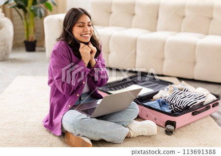 Smiling woman with laptop and open suitcase 113691388