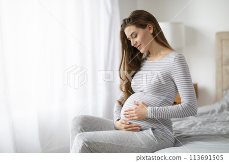 Expectant mother sitting thoughtfully at home, copy space 113691505
