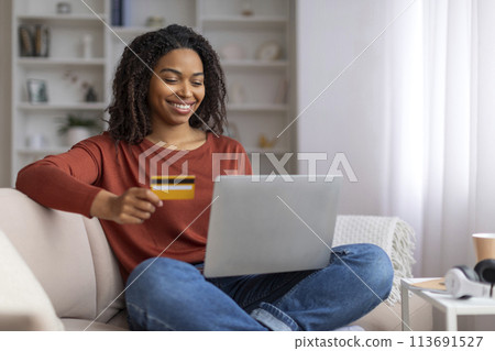 Cheerful young black woman using credit card for online shopping on laptop Cheerful young black woman using credit card for online shopping on laptop 113691527