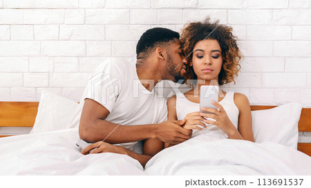 Couple with man kissing while on phone Couple with man kissing while on phone 113691537