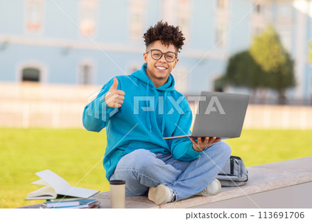 Student giving thumbs up with laptop, studying at park 113691706