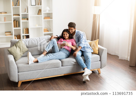 Hindu couple cuddling on couch looking at phone together 113691735