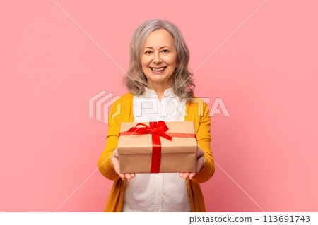 Elegant retired mature lady poses giving wrapped present box, studio 113691743