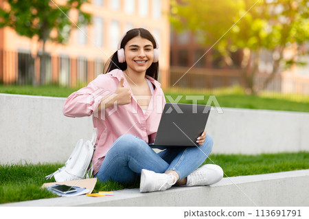Girl giving thumbs up with laptop outside Girl giving thumbs up with laptop outside 113691791