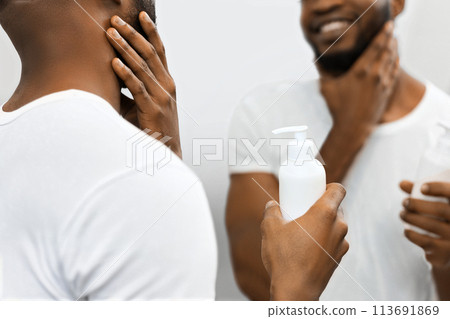 Man holding lotion bottle, smiling at reflection in bathroom Man holding lotion bottle, smiling at reflection in bathroom 113691869