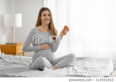 Pregnant woman with an apple on the bed 113691918