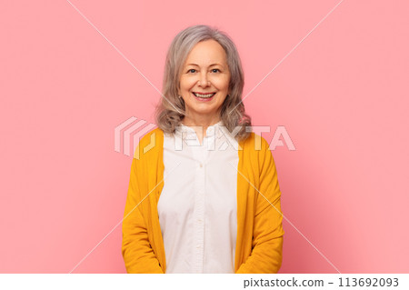 Cheerful senior lady with gray hair poses against pink backdrop 113692093