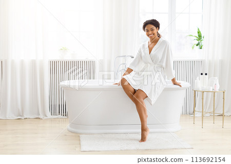 Relaxed woman sitting on edge of a modern bathtub Relaxed woman sitting on edge of a modern bathtub 113692154