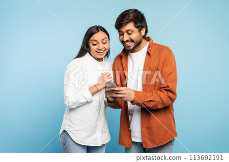 Excited indian couple looking at mobile phone using application, studio 113692191