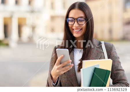Student with glasses browsing phone smiling at university campus 113692329