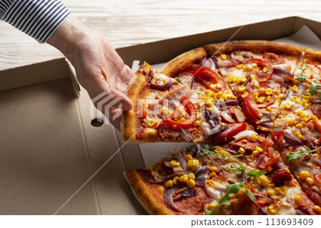 Human caucasian hand takes slice of large pizza from carton box on white wooden table 113693409