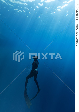 Freediver Swimming in Deep Sea With Sunrays. Young Man Diver Eploring Sea Life. 113695162