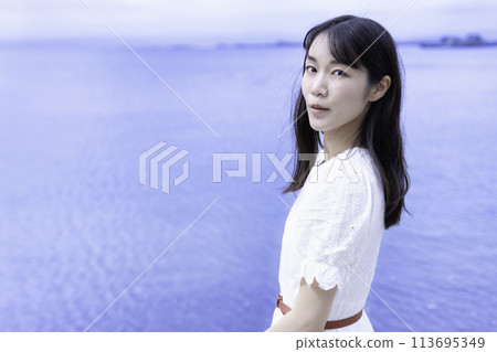 A woman in a white dress strolling by the sea A woman in a white dress strolling by the sea 113695349