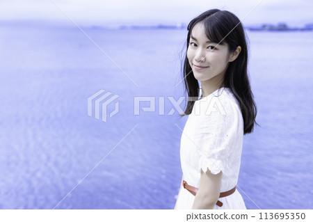 A woman in a white dress strolling by the sea A woman in a white dress strolling by the sea 113695350