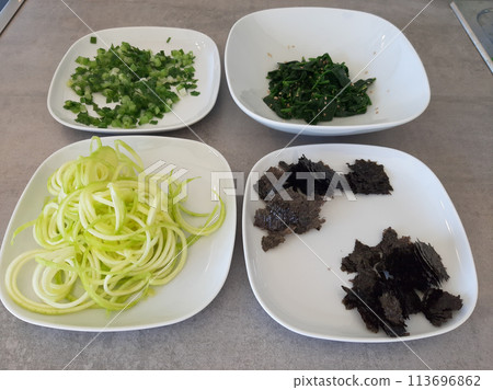 Homemade side dish with spinach, zucchini spirals, spring onions and chopped nori algae served on white plates 113696862
