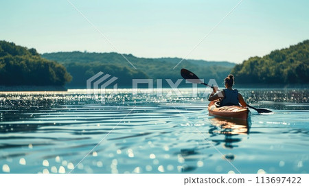 Person kayaking on a tranquil lake with shimmering waters, surrounded by lush hills 113697422