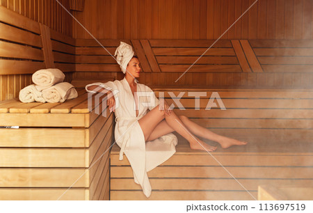 Young woman relaxing and sweating in hot sauna wrapped in towel. Girl In Sauna. Interior of Finnish sauna, classic wooden steam room with hot steam. Russian bathroom. Relax in hot Bathhouse with steam Young woman relaxing and sweating in hot sauna wrapped in towel. Girl In Sauna. Interior of Finnish sauna, classic wooden steam room with hot steam. Russian bathroom. Relax in hot Bathhouse with steam 113697519