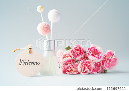 Fragrance diffuser with welcome tag and pink flowers on vintage blue background 113697611