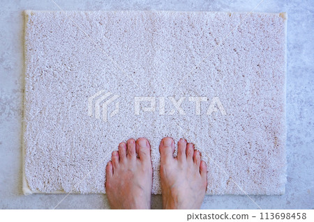 Woman drying her feet on a bath mat 113698458