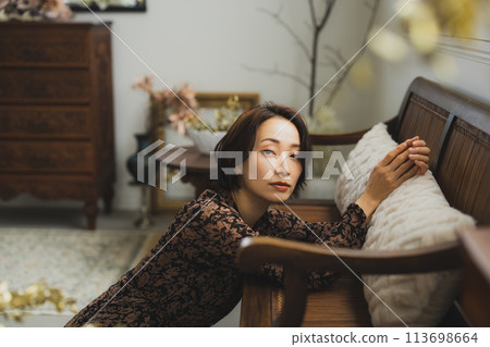 Middle-aged woman sitting on a sofa in a room Middle-aged woman sitting on a sofa in a room 113698664