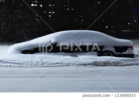 A car covered with snow on a night city winter street. A car covered with snow on a night city winter street. 113698833