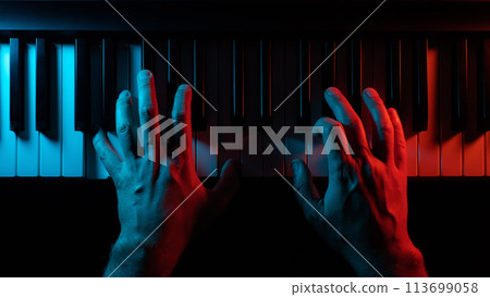 Close-up hands of a pianist playing a keyboard instrument (piano, grand or synth) in a red and blue backlight. Concept of scary dramatic music from horror movie. 113699058