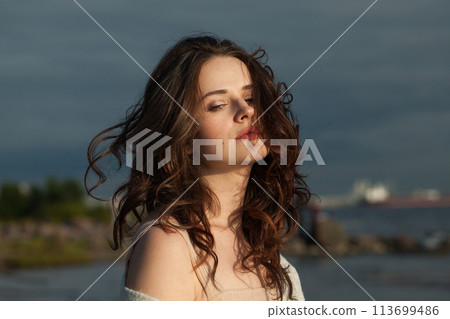 Sensual young woman model with brown hair and natural make-up walking along the shore of the resort  113699486