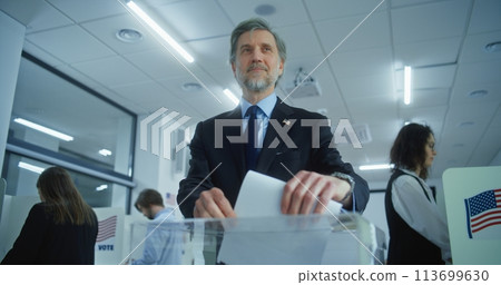 Mature US businessman or politician puts ballot in box after voting Mature US businessman or politician puts ballot in box after voting 113699630