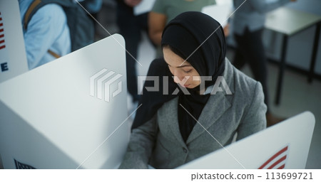 Muslim woman in hijab votes in booth in modern polling station Muslim woman in hijab votes in booth in modern polling station 113699721