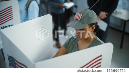 Female American army soldier votes in booth in modern polling Female American army soldier votes in booth in modern polling 113699731