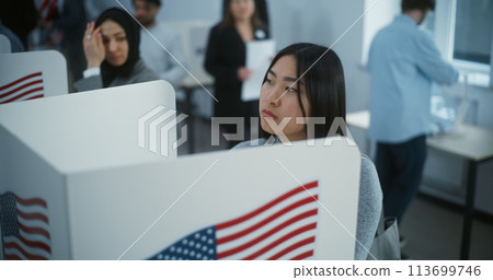 Asian female American citizen votes in booth in polling station 113699746