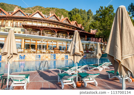 Seaside resort with pool and comfortable lounge chairs with folded sun parasols 113700134