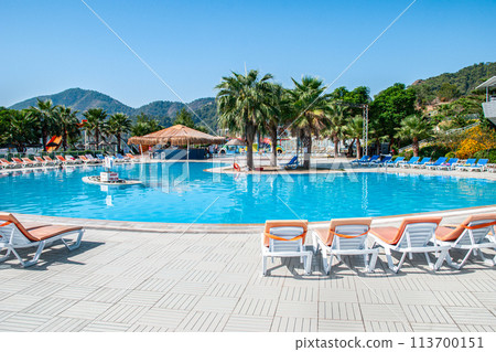 Circular swimming pool surrounded by lounge chairs and a bar with a thatched roof 113700151