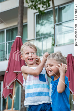 Two little boys are laughing and playfully holding each others ears 113700175
